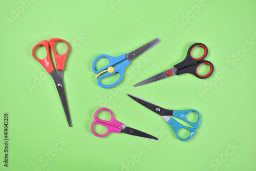 Red, green blue, pink and black scissors scattered on green background