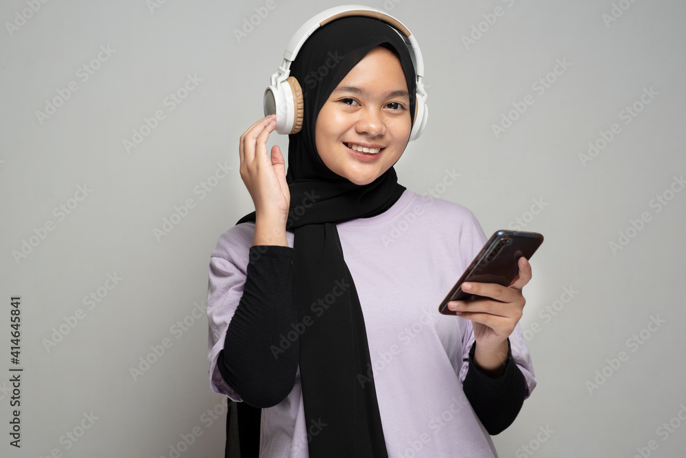 Young happy asian muslim woman holding mobile phone and enjoing using headphone to listen the music Young happy asian muslim woman holding mobile phone and enjoing using headphone to listen the music