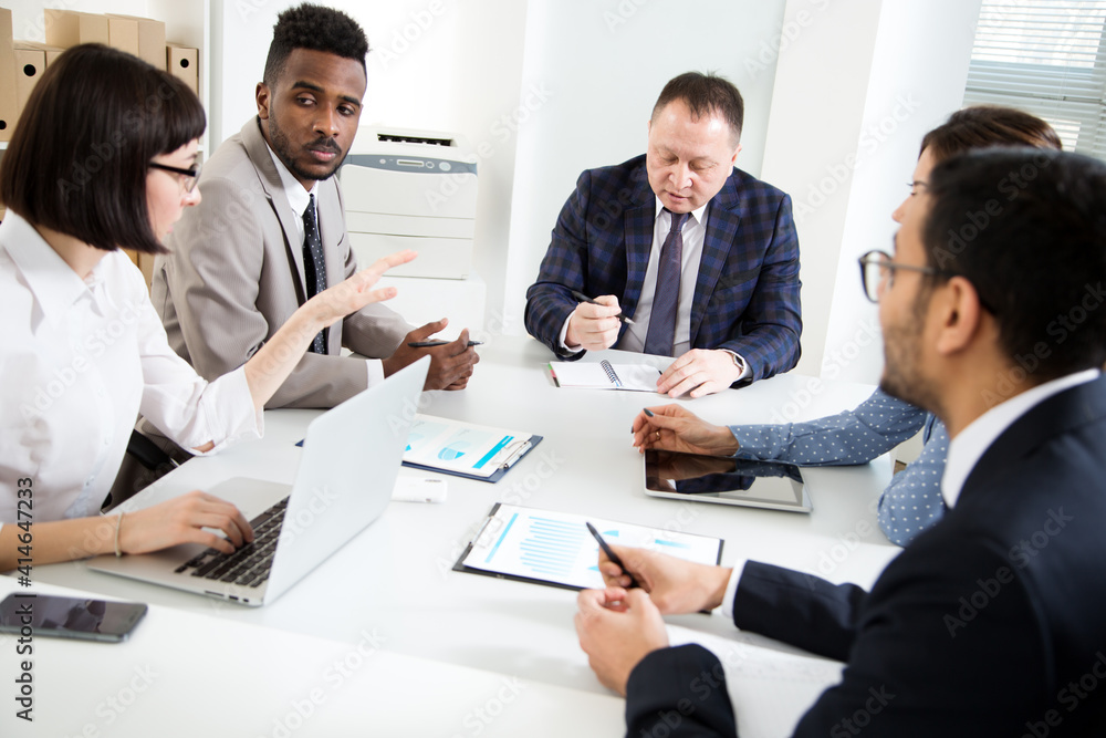 Group of multi-ethnic business people sitting around the office desk and discussing the project Group of multi-ethnic business people sitting around the office desk and discussing the project