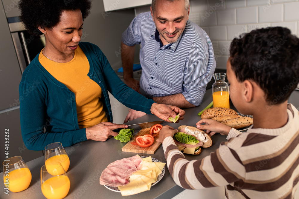 Smiling mixed race family with they son standing in the kitchen preparing sandwich for breakfast at home. Smiling mixed race family with they son standing in the kitchen preparing sandwich for breakfast at home.