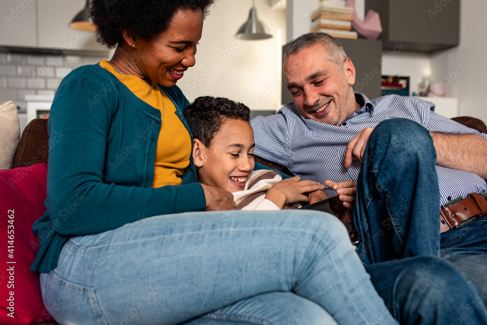 Smiling mixed race family enjoying time at home sitting on sofa in living room looking at tablet. Smiling mixed race family enjoying time at home sitting on sofa in living room looking at tablet.