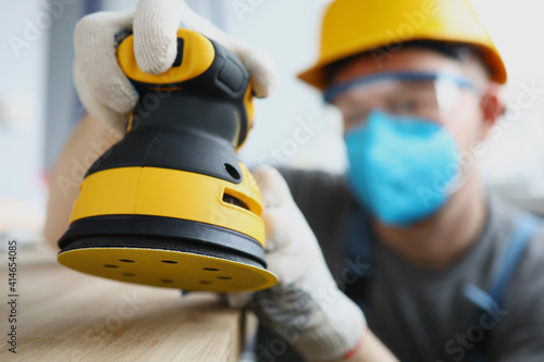 Master builder in protective mask is holding disc sander. Renovation services concept photo