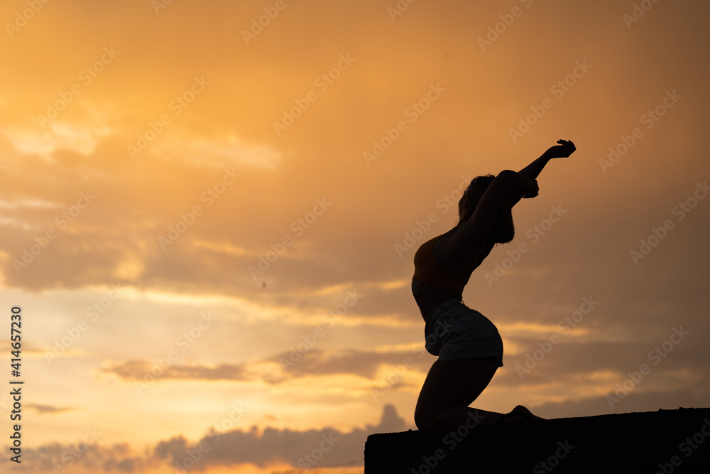 Fototapeta premium Flexible girl doing exercise on sky background during dramatic sunset