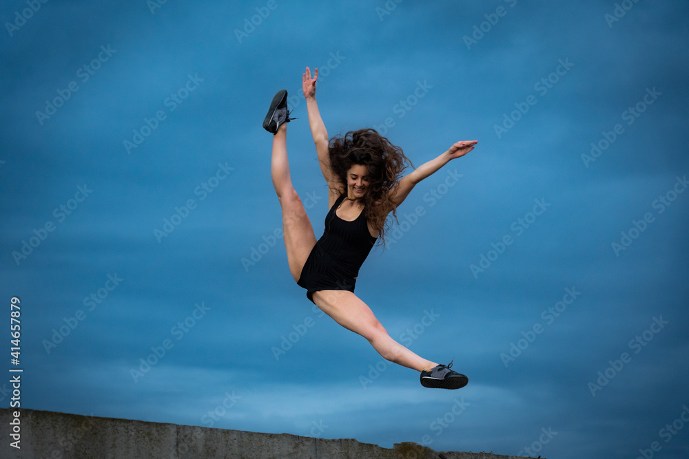 Fototapeta premium Super flexible woman jumping on the sky background. Concept of healthy lifestyle, happiness and joy