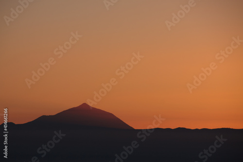 Silhouette of the Teide volcano backlit at sunset seen from Gran Canaria in warm orange tones