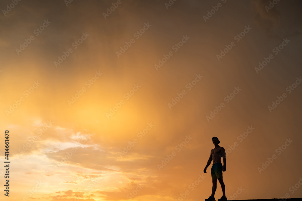Man on the edge of cliff standing over dramatic sky during sunset .concept of thinking, meditation and concern