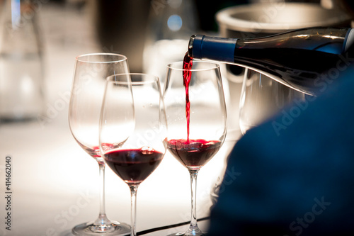 close up on a wine glasses, bottle and red wine being poured