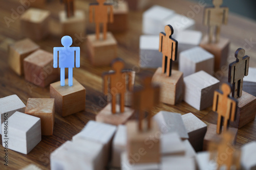 Wooden men on wooden cubes of brown color, one of them is blue. How to stand out among people and be an example to others concept