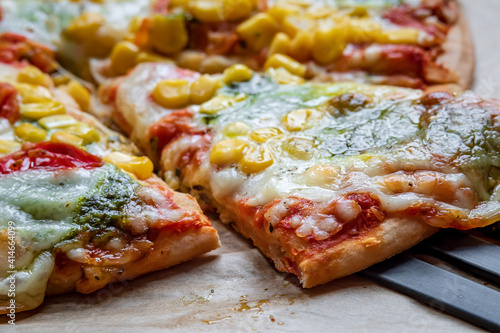 Close up on colorful fresh pizza hot from the oven with mozzarella cheese, corn, pesto and cherry tomatoes. Baked, delicious, gluten free pizza sliced and placed on a baking sheet. Ready to be served.