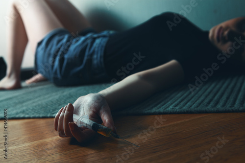 the girl lies on the floor and holds a syringe in her hands