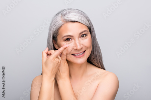 Portrait of attractive cheery naked nude gray-haired lady inserting lens isolated over grey pastel color background