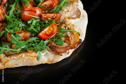 Pinsa romana gourmet italian cuisine on black background. Scrocchiarella traditional dish. Food delivery from pizzeria. Pinsa with meat, arugula, tomatoes, cheese.