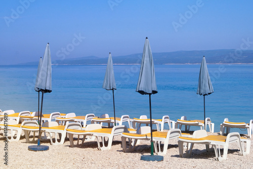 Blue umbrellas and chaises for relax on sea coast. Summer vacations and travel concept. Paid service on beaches.