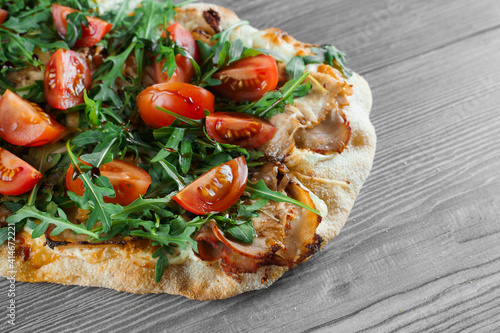 Scrocchiarella gourmet italian cuisine on grey wooden background. Pinsa romana traditional dish. Food delivery from pizzeria. Pinsa with meat, arugula, tomatoes, cheese.