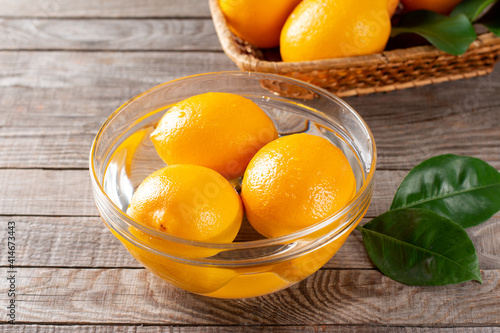 Fresh ripe lemons in a glass bowl with water on a wooden table