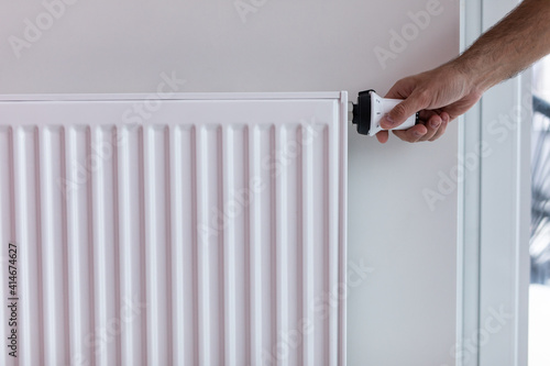 Youmg woman holding temperature knob of heating radiator