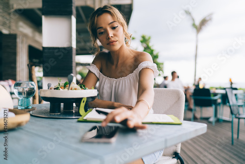 Young woman on holidays sitting in cafe and checking notifications on mobile phone