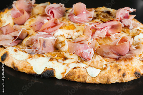 Scrocchiarella with pear, cheese, prosciutto on black background. Pinsa romana gourmet italian cuisine. Food delivery from pizzeria. Junk food photo