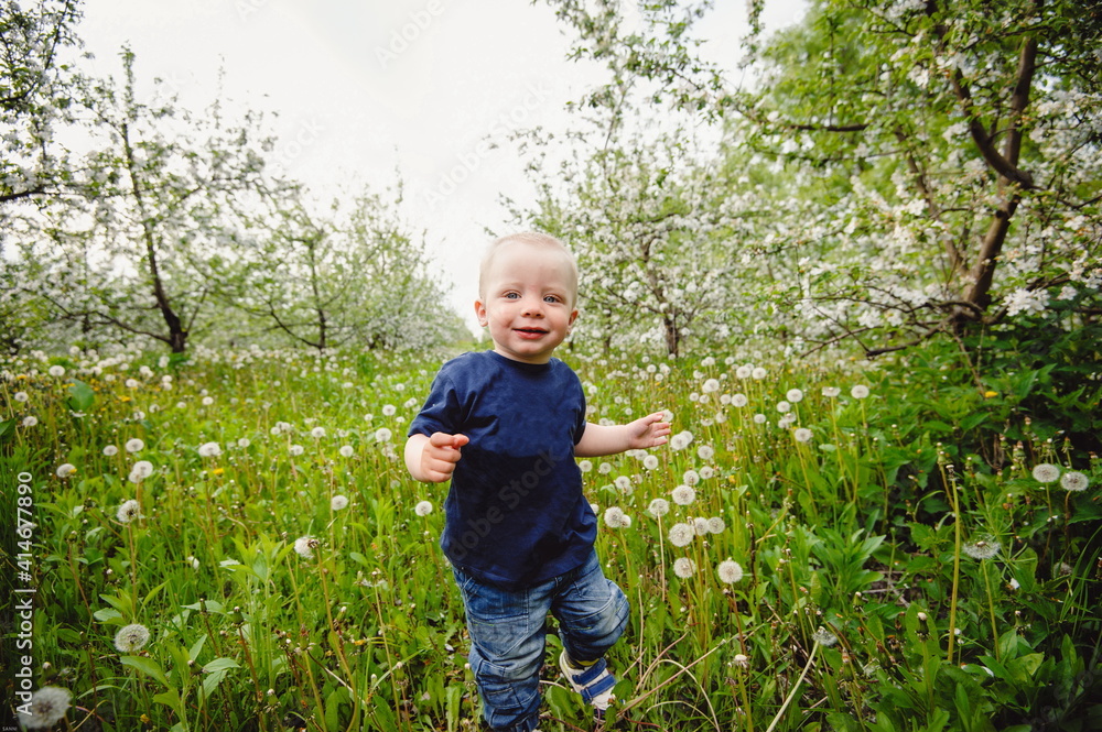 The one-year-old boy is making some of his first steps outdoors in the spring garden. Stylish baby boy having fun outside in the park. Concept of happy family or successful adoption or parenting. The one-year-old boy is making some of his first steps outdoors in the spring garden. Stylish baby boy having fun outside in the park. Concept of happy family or successful adoption or parenting.