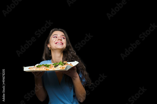 Woman courier with pinsa romana gourmet italian cuisine on black background. Holding scrocchiarella traditional dish. Food delivery from pizzeria. Pinsa with meat, arugula, olives, cheese. photo