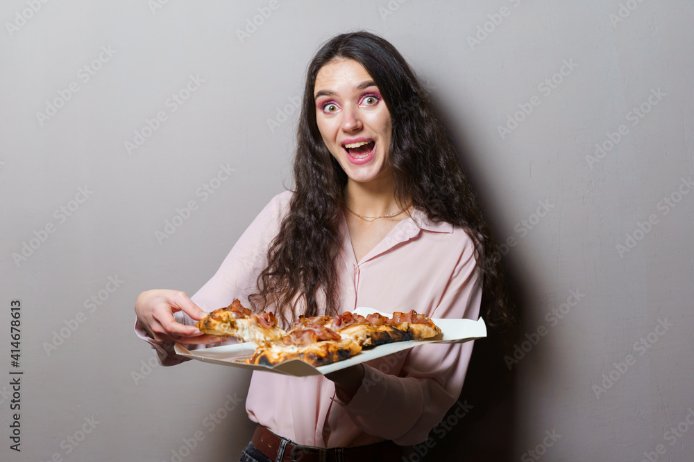 Girl courier with pinsa romana gourmet italian cuisine on grey background. Holding scrocchiarella traditional dish. Food delivery from pizzeria. Pinsa with meat, arugula, olives, cheese. Girl courier with pinsa romana gourmet italian cuisine on grey background. Holding scrocchiarella traditional dish. Food delivery from pizzeria. Pinsa with meat, arugula, olives, cheese.