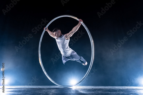 Cyr Wheel circus artist on smoked, dark background performing on stage 