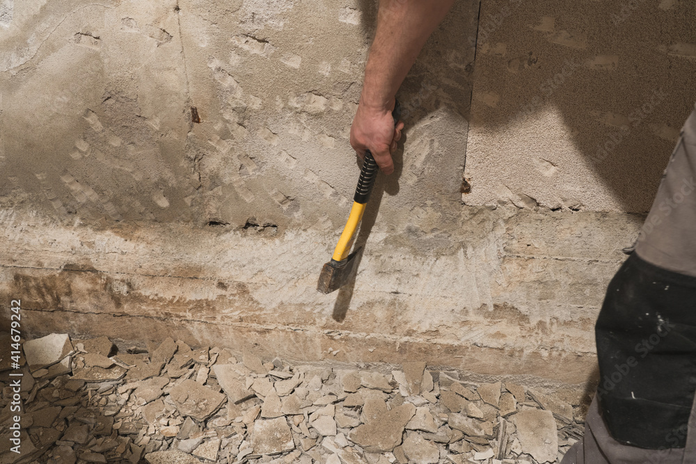 A builder using an axe to remove walls plaster.
