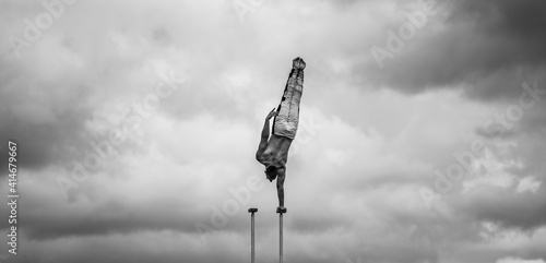 Flexible male circus Artist keep balance by one hand against amazing cloudscape. Individuality, outstanding and originality. photo