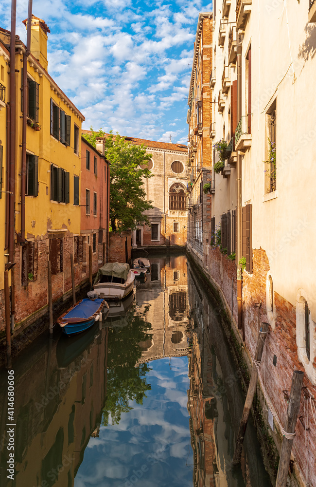 View of quiet street and narrow canal with boats along brink. The residential area of Venice, Italy.