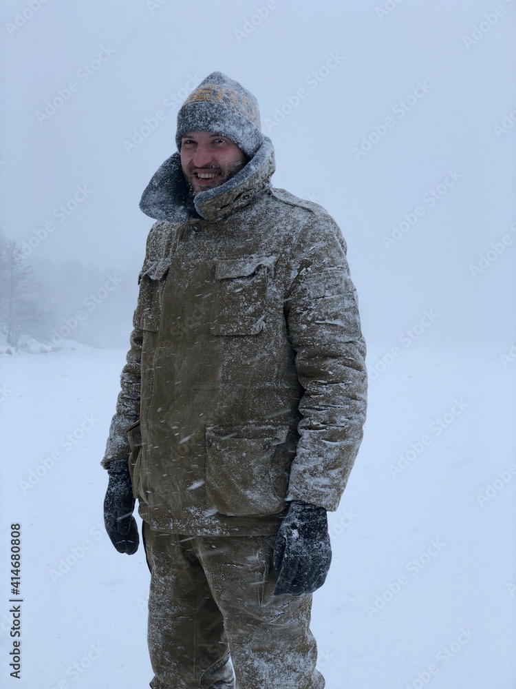 Naklejka premium smiling frozen man in the snow looking at the camera in the winter forest after a snow storm immunity and cold