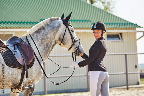 Beautiful horse rider girl stands near a horse on a farm   