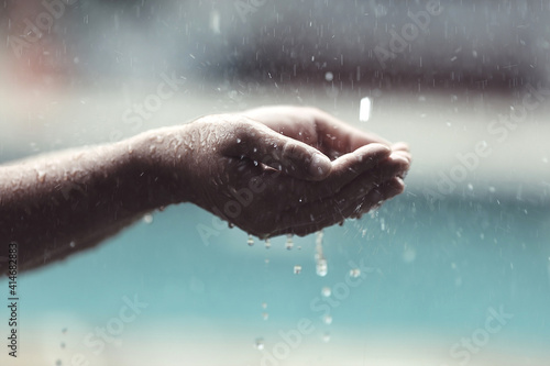 Male hand play catching rain drops on blurred grey background. Pure rainy spring weather joy under waterfall splash, rain season © asauriet