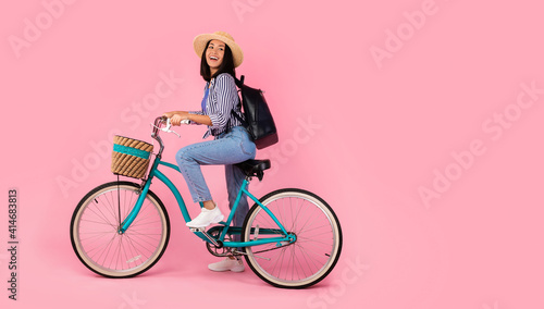 Excited asian woman riding retro bicycle with wicker basket © Prostock-studio