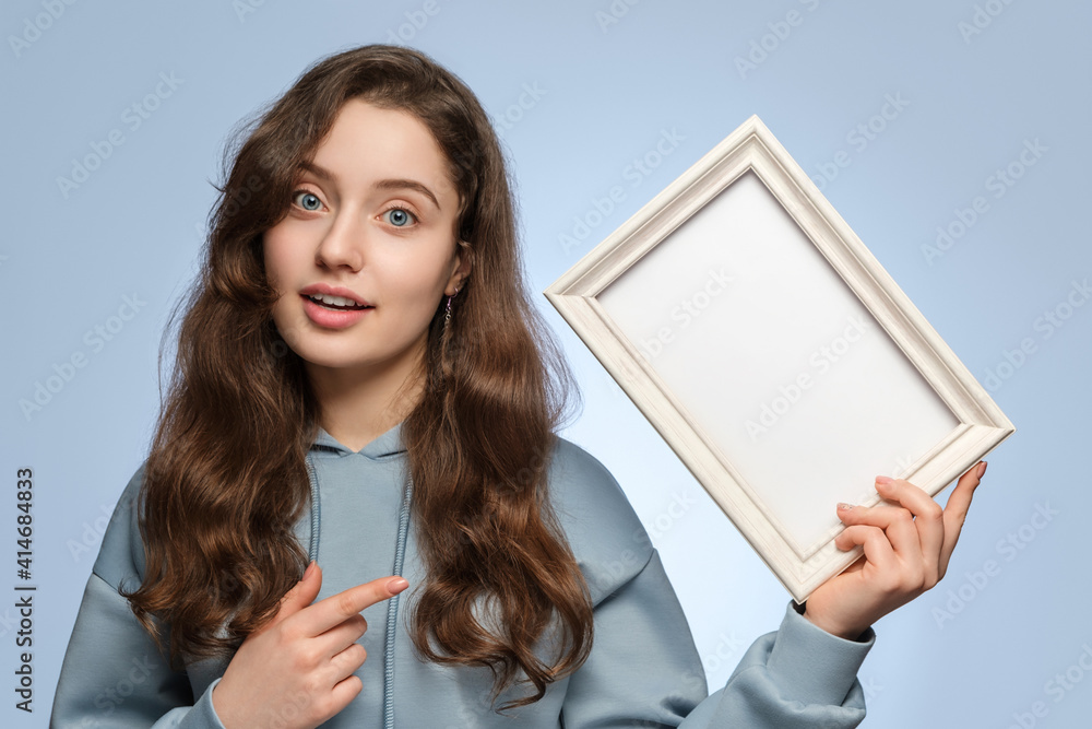 Young Woman With An Empty Picture Frame In Her Hand On A Light Blue
