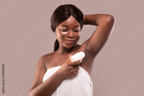 Obraz na plátně Portrait of smiling black woman applying roller deodorant to armpit zone