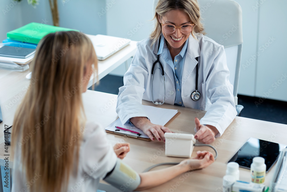 Obraz premium Shot of mature beautiful female doctor measuring heart and blood pressure while taking care to young patient in the medical consultation.