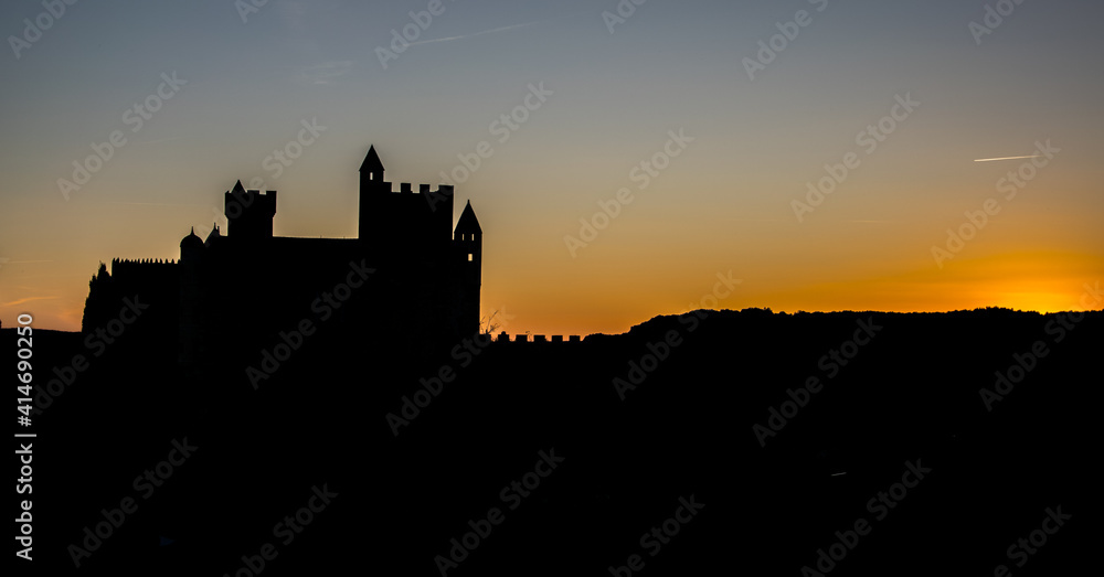 Castillo medieval francés recortándose al atardecer sobre el cielo dorado