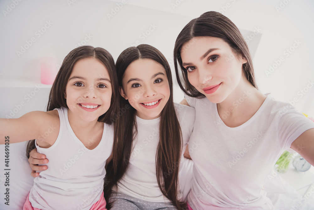 Photo of adorable sweet three siblings nightwear sitting bed smiling hugging tacking selfie indoors inside room home Photo of adorable sweet three siblings nightwear sitting bed smiling hugging tacking selfie indoors inside room home