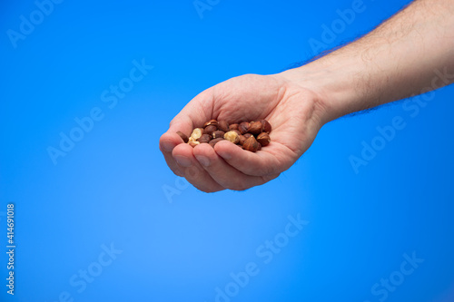 Group of various nuts held in palm by Caucasian male hand isolated on blue background studio shot