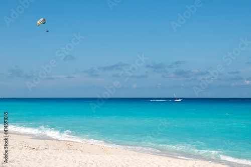 Parasailing on the tropical sea near an exotic beach in Cancun, Mexico. Summer fun and recreation activities. In the background the blue sky and few clouds