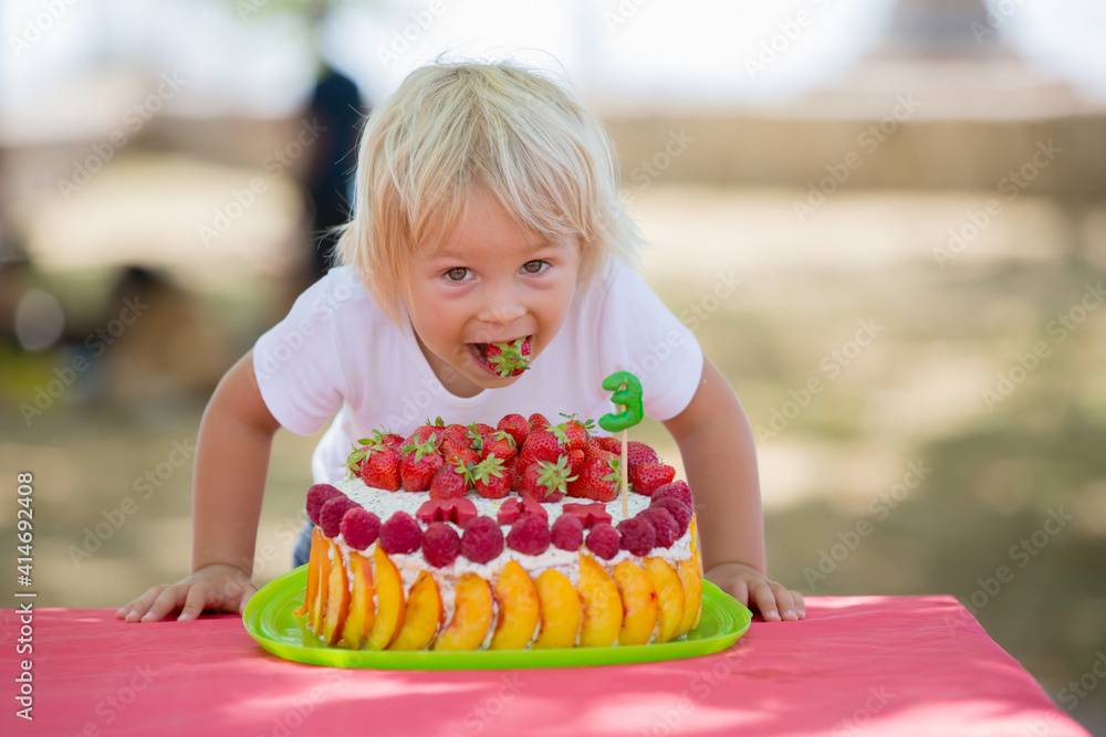 Sweet little blond toddler boy, celebrating his third birthday in a park with siblings and friends Sweet little blond toddler boy, celebrating his third birthday in a park with siblings and friends