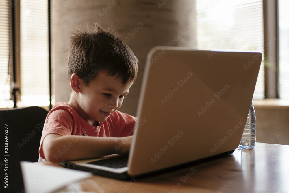 Portrait of cute smiling little boy sitting on office chair behind desk in the office. Happy boy using laptop. Portrait of cute smiling little boy sitting on office chair behind desk in the office. Happy boy using laptop.