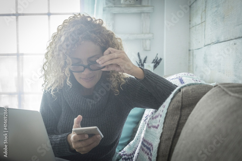 Young woman at home use cellular phone and laptop computer sitting on the sofa - modern people and technology device - social life and online lifestyle concept - smart working or leisure indoor photo