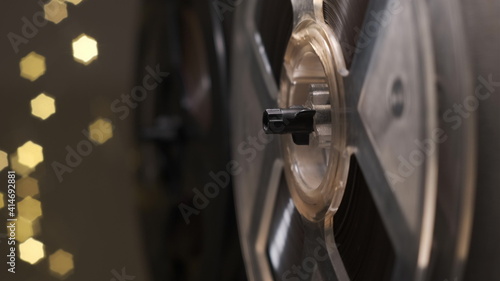 Old fashion vintage reel tape recorder. Reel film tape rotating on vintage professional player with lights on background. close up of spool of music player. © Vit
