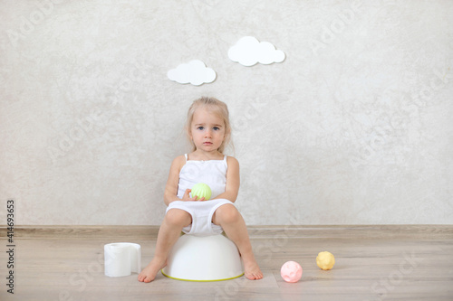 A little baby girl is sitting on a potty.