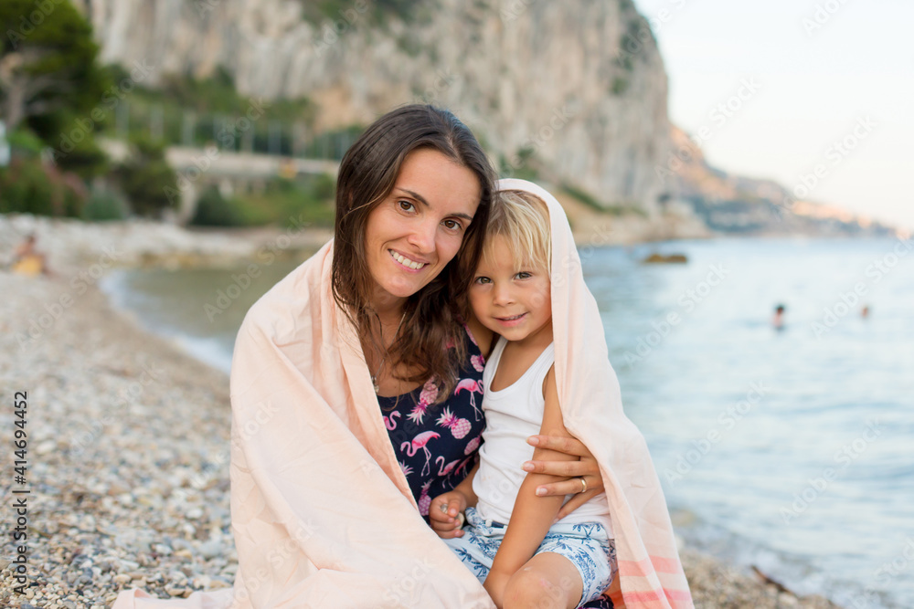 Loving mother and son, blond toddler boy, hugging at the beach, enjoying time