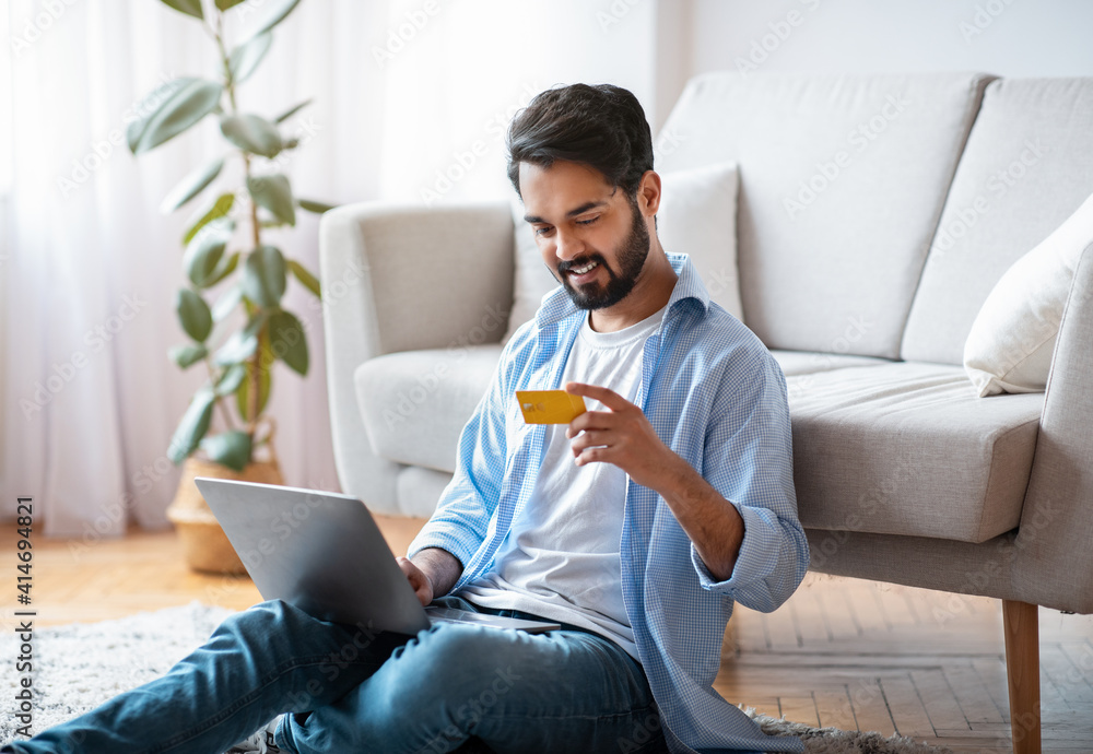 Millennial Arab Guy Making Payments With Laptop And Credit Card At Home Millennial Arab Guy Making Payments With Laptop And Credit Card At Home