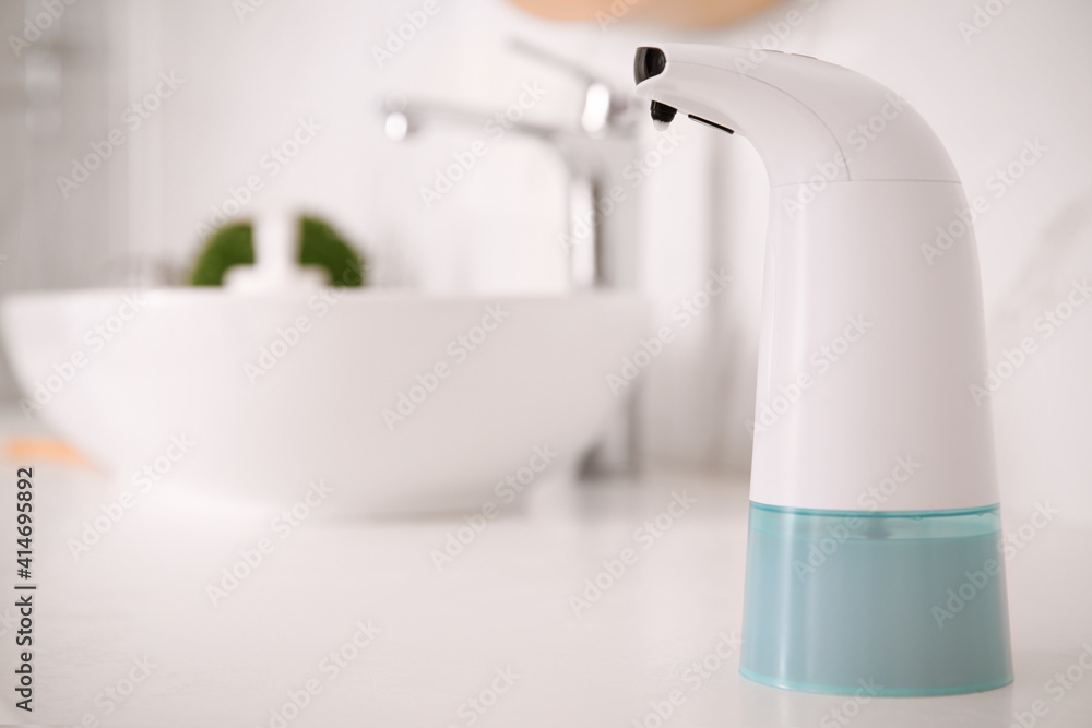 Modern automatic soap dispenser on countertop in bathroom. Space for text Modern automatic soap dispenser on countertop in bathroom. Space for text