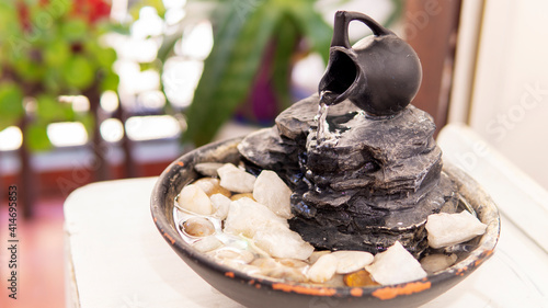 Close view of a decorative zen water fountain next to a few green plants on a warm summer morning