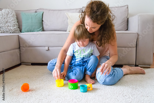 Single mother playing with disabled child with down syndrome in their living room at their apartment